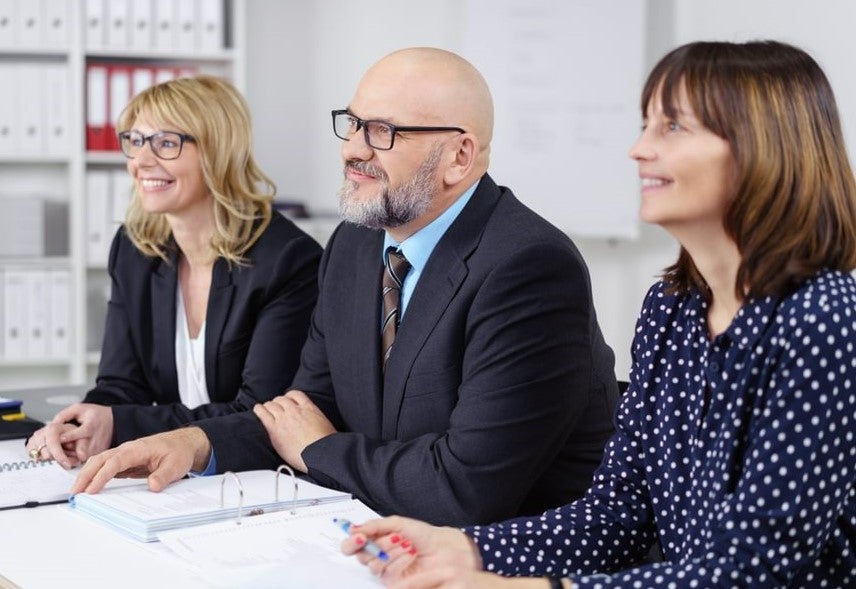 three business people, sitting at a desk and facing the same direction